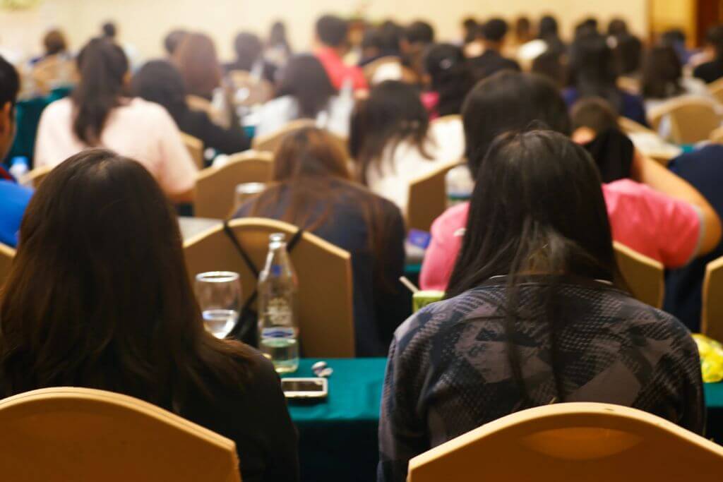 Audience members seated in a conference room attending a professional training session. The image includes the text "Online and Onsite Singapore Math Group Teacher Training" and highlights Singapore Math Teacher Training and Professional Development opportunities offered by Mindset 4 Math for educators in both online and in-person formats. This training is offered in the Philippines, Asia, Canada, the United States, Europe, the UK, and all over the world.